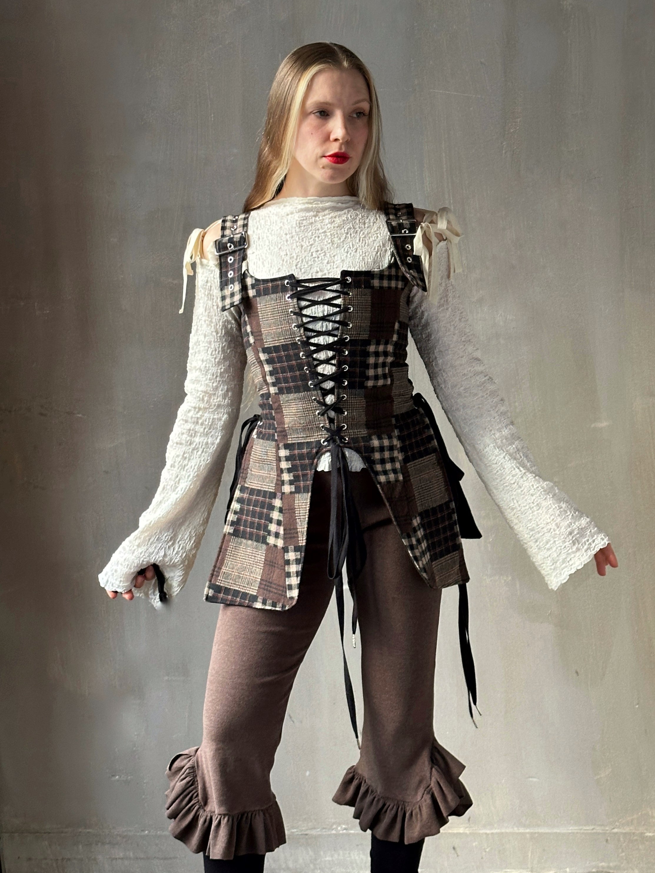 Person wearing a plaid elongated corset vest in patchwork brown.